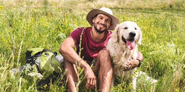 Viaggiatore seduto con cane golden retriever su prato verde — Foto stock