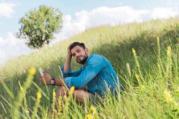 Male traveler using smartphone on green summer meadow with tree — Stock Photo