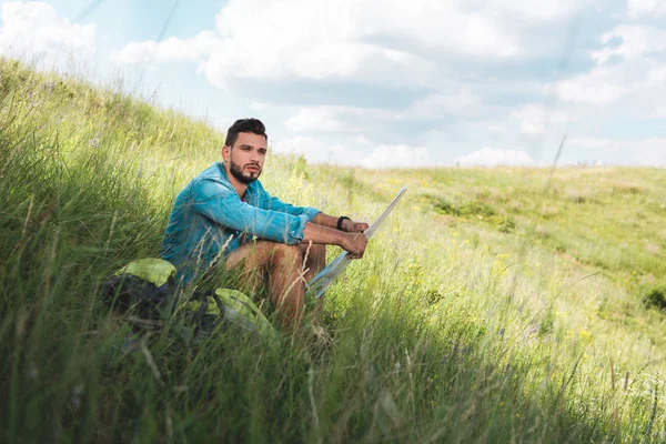 Чоловік мандрівник сидить з рюкзаком і на карті на зеленому лузі — стокове фото