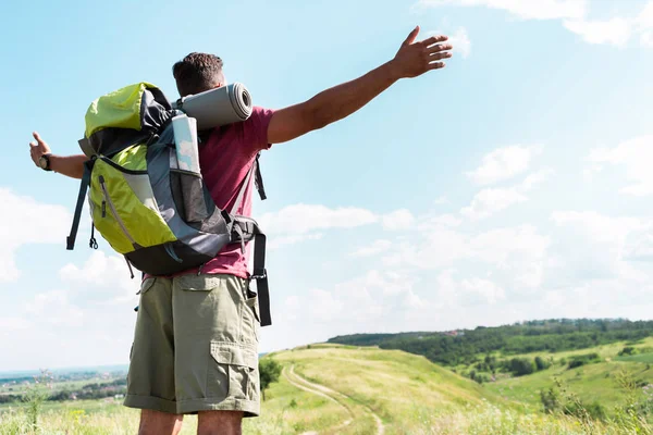 Tourist mit Rucksack steht mit ausgestreckten Händen auf Sommerwiese bei bewölktem Himmel — Stockfoto
