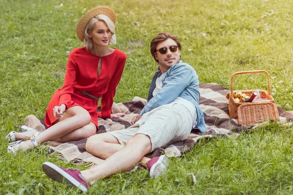 Couple assis sur la couverture dans le parc et regardant loin — Photo de stock