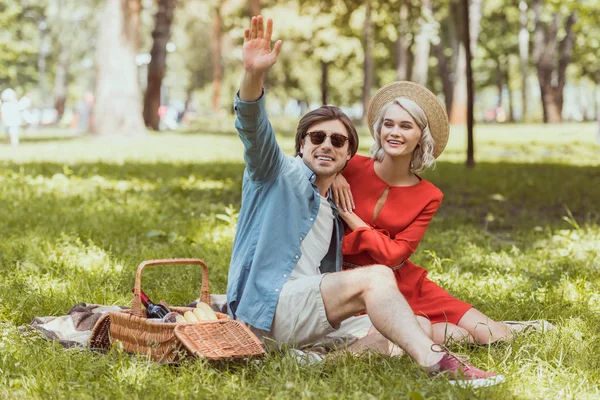 Namorado sentado em cobertor no parque e mão acenando — Fotografia de Stock