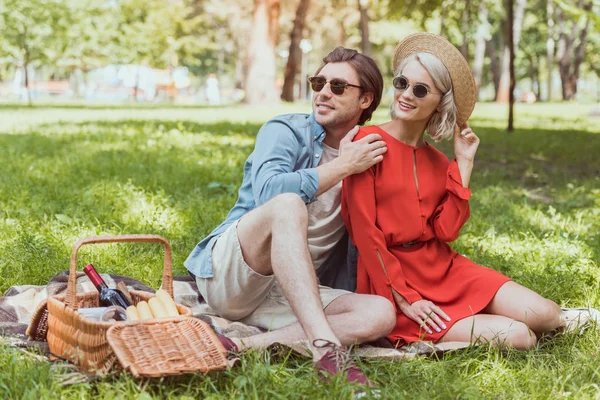 Pareja sentada y abrazándose en manta en parque - foto de stock