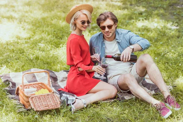 Fidanzato versando vino rosso in bicchieri al picnic nel parco — Foto stock