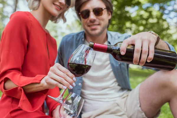 Imagem cortada de namorado derramando vinho tinto em copos no parque — Fotografia de Stock