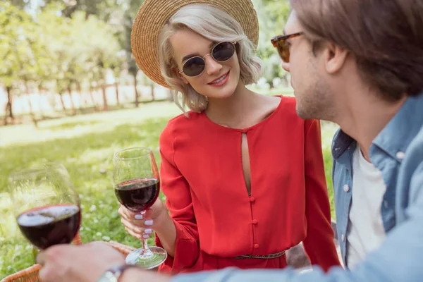 Casal em óculos de sol segurando copos de vinho tinto no parque — Fotografia de Stock