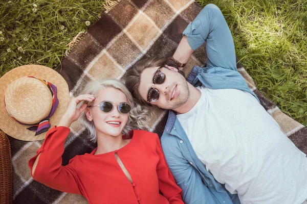 High angle view of couple in sunglasses lying on blanket in park — Stock Photo