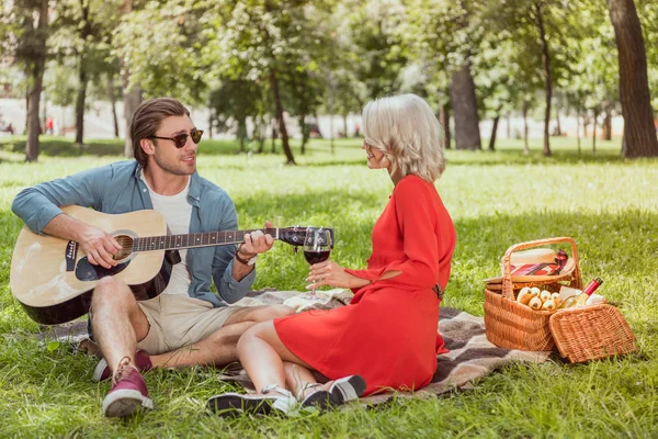 Красивый парень играет на гитаре для девушки на пикнике — стоковое фото