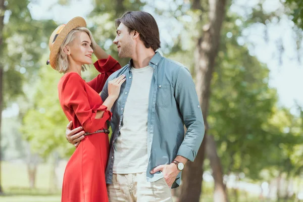 Lächelnde Freundin und Freund kuscheln im Park und schauen einander an — Stockfoto