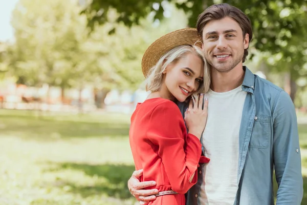 Sorrindo casal abraçando no parque e olhando para a câmera — Fotografia de Stock