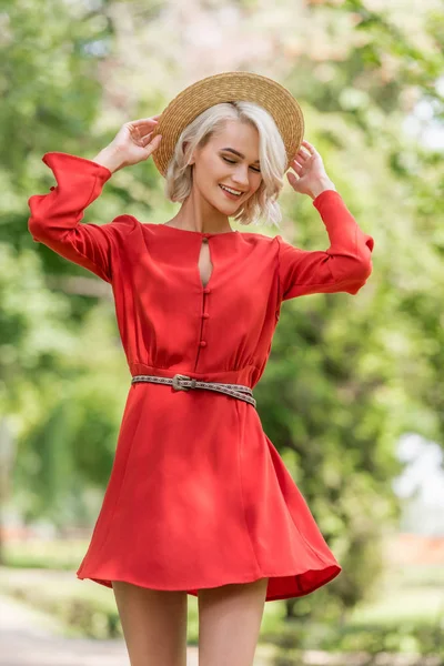 Stylish attractive girl in red dress and straw hat posing in park — Stock Photo