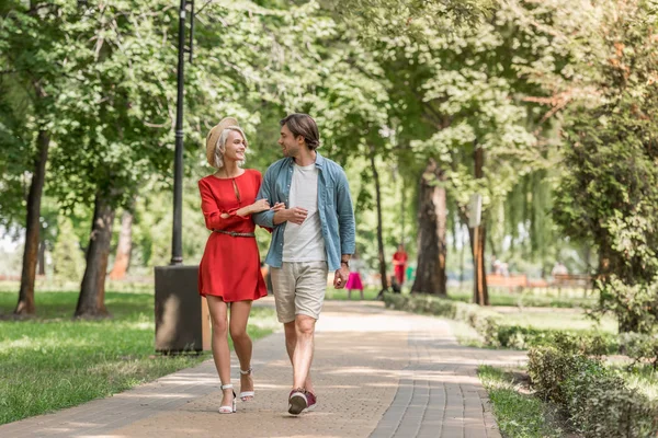 Sorrindo namorada e namorado andando juntos no parque e olhando um para o outro — Stock Photo