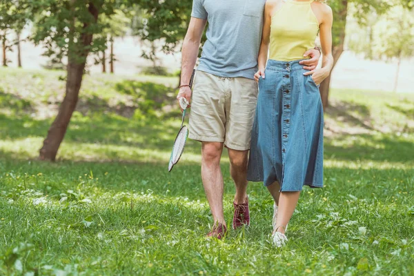 Imagen recortada de pareja caminando con raquetas de bádminton y lanzadera para jugar en el parque - foto de stock