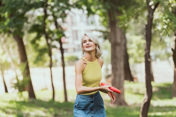 Atractiva chica rubia lanzando disco de frisbee en el parque - foto de stock