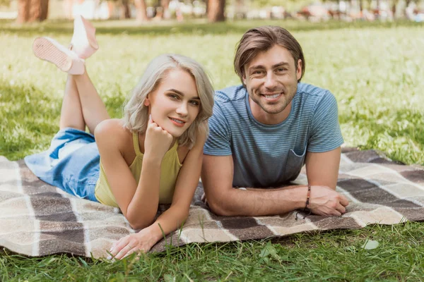 Пара лежит на одеяле в парке и смотрит в камеру — стоковое фото