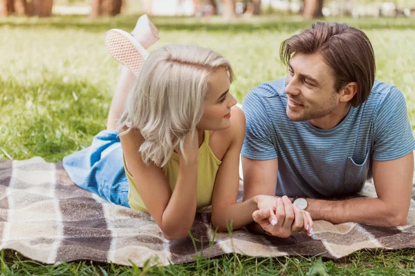 Couple lying on blanket in park and holding hands — Stock Photo