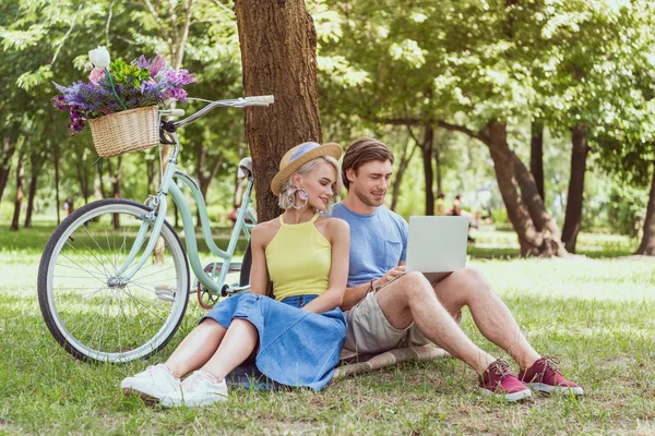 Coppia seduta vicino all'albero nel parco e utilizzando il computer portatile — Foto stock