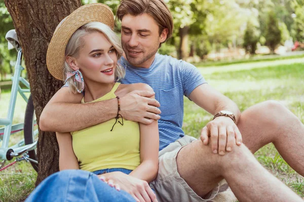 Novio abrazando novia en paja sombrero en parque - foto de stock