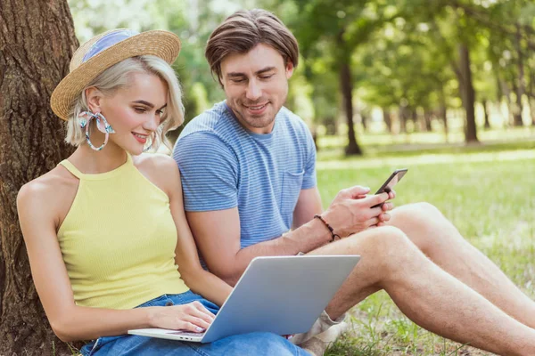 Coppia guardando il computer portatile e seduto sull'erba nel parco — Foto stock