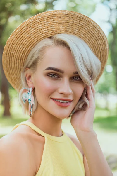 Portrait of attractive blonde girl in straw hat looking at camera in park — Stock Photo