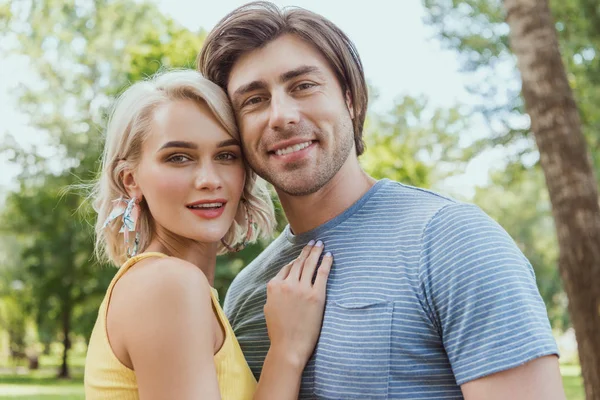 Couple souriant embrasser et regarder la caméra dans le parc — Photo de stock