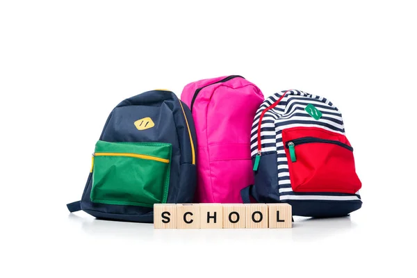 Три цветные школьные сумки и деревянные кубики со словом школа изолированы на белом — стоковое фото