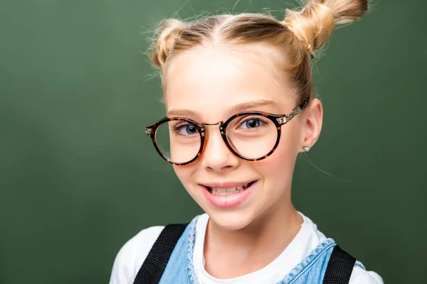 Portrait of adorable schoolchild in glasses looking at camera near blackboard — Stock Photo