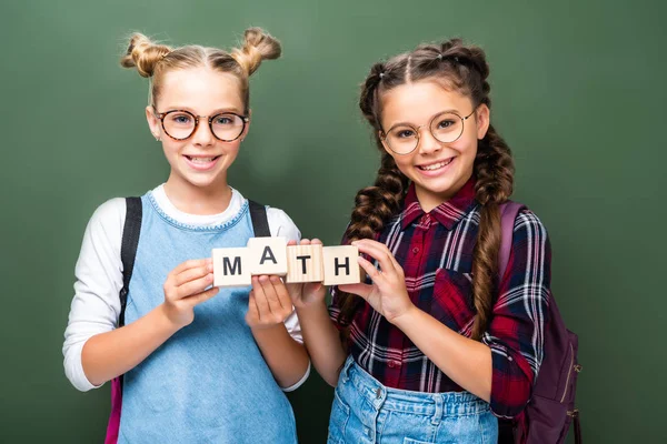 Escolares sosteniendo cubos de madera con palabras matemáticas cerca de pizarra - foto de stock