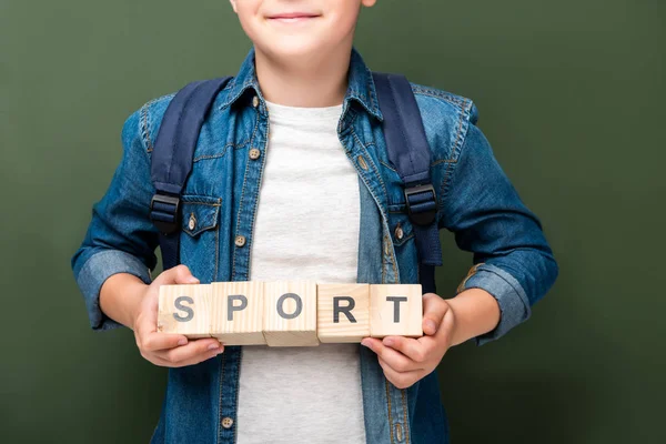 Cropped image of schoolboy holding wooden cubes with word sport near blackboard — Stock Photo