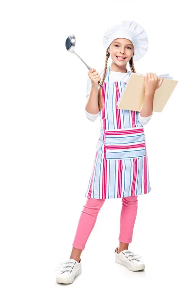 Écolier souriant en costume de chef tenant louche et livre de cuisine isolé sur blanc — Photo de stock