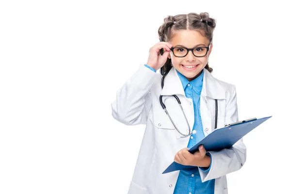 Schoolchild in costume of doctor holding clipboard and touching glasses isolated on white — Stock Photo