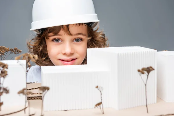 Scolaro in costume di architetto vicino modello di edifici isolati su bianco — Foto stock