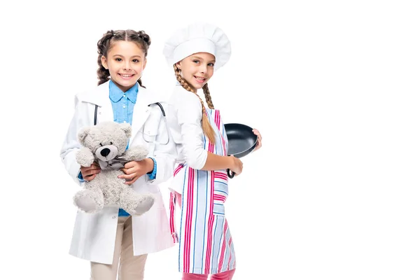 Escolares con disfraces de médico y chef de pie en bata blanca y delantal aislado en blanco - foto de stock