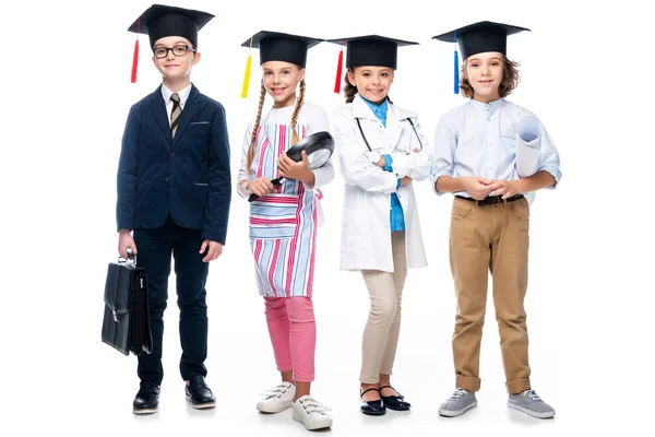 Escolares con disfraces de diferentes profesiones y gorras de graduación mirando a la cámara aislada en blanco - foto de stock