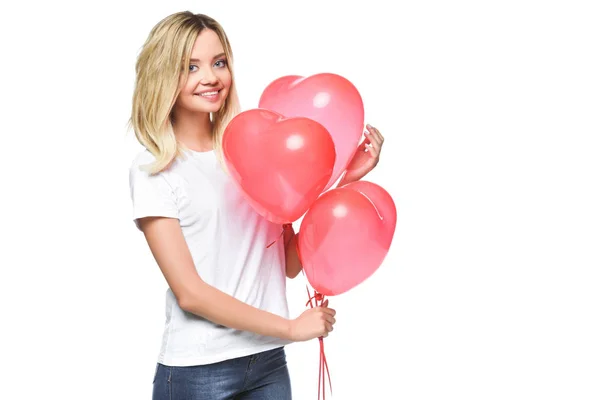 Sorridente ragazza attraente in camicia bianca contenente fascio di palloncini a forma di cuore isolato su bianco — Foto stock