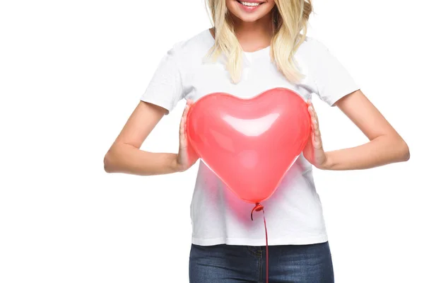 Imagen recortada de niña sonriente en camisa blanca sosteniendo globo en forma de corazón aislado en blanco - foto de stock