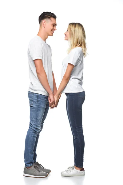 Vista laterale di coppia sorridente che si tiene per mano e si guarda isolato su bianco — Foto stock