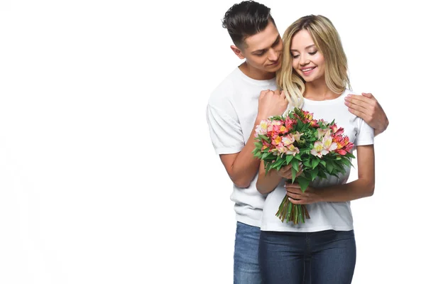 Boyfriend hugging girlfriend and she holding bouquet of flowers isolated on white — Stock Photo