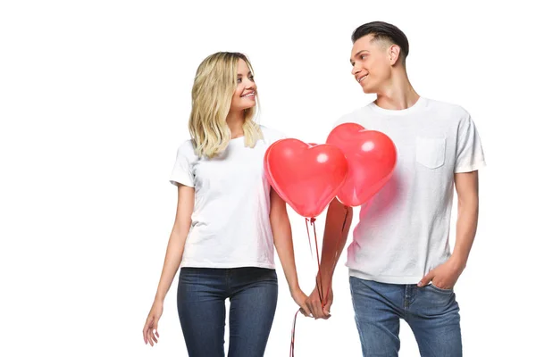 Couple standing with bundle of heart shaped balloons and looking at each other isolated on white — Stock Photo