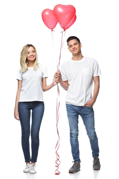 Pareja de pie con un paquete de globos en forma de corazón y mirando a la cámara aislada en blanco - foto de stock