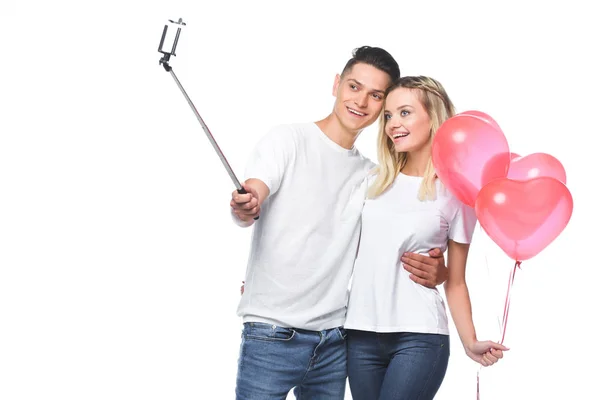 Couple with balloons taking photo with smartphone and selfie stick isolated on white — Stock Photo
