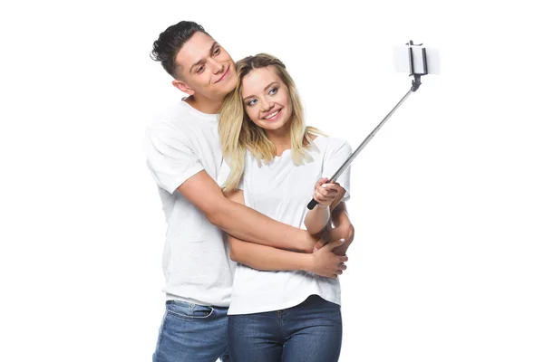 Feliz pareja tomando fotos con teléfono inteligente y selfie stick aislado en blanco - foto de stock
