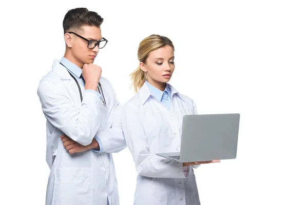 Jóvenes médicos pensativos en batas blancas utilizando el ordenador portátil, aislado en blanco - foto de stock