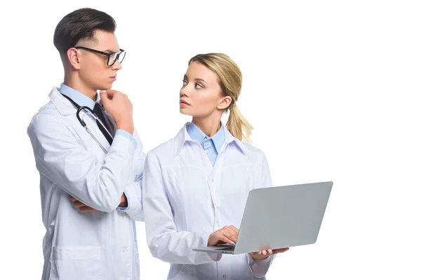 Nachdenkliche Ärzte mit Laptop, die sich gegenseitig anschauen, isoliert auf weiß — Stockfoto