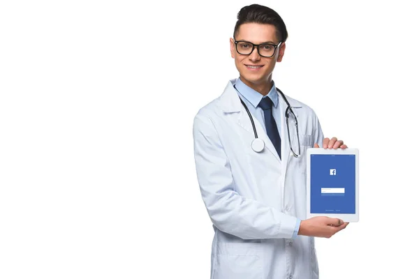 Beau jeune médecin tenant tablette avec application facebook à l'écran isolé sur blanc — Photo de stock