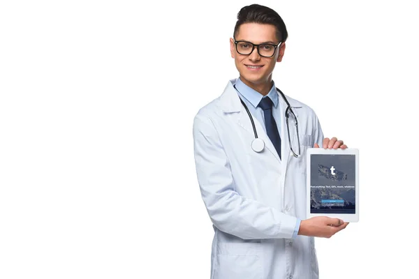Bonito jovem médico segurando tablet com aplicativo tumblr na tela isolado no branco — Fotografia de Stock