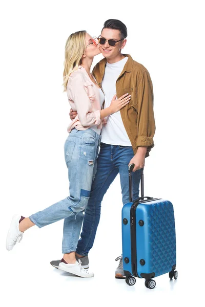 Красива молода жінка цілує свого хлопця, стоячи з валізою ізольовано на білому — стокове фото