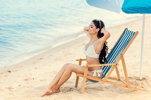 Jolie fille assise sur une chaise de plage sous un parapluie près de la mer — Photo de stock