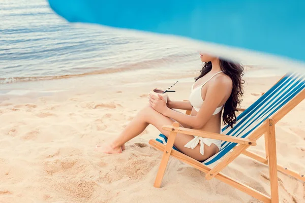Приваблива дівчина сидить на пляжному стільці з кокосовим коктейлем — стокове фото