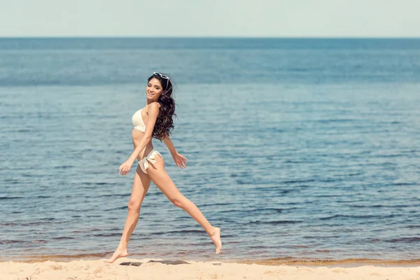 Happy slim young woman in white bikini jumping on sea beach — Stock Photo